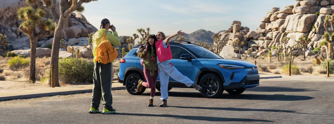 Man taking a photo of two women in front of the2026 Toyota Corolla Cross in the desert